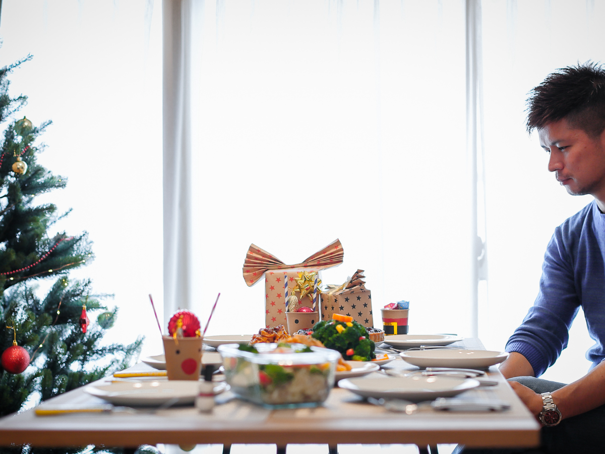 Man sitting alone at a Christmas table with food, gifts, and decorations, reflecting during the holiday season.