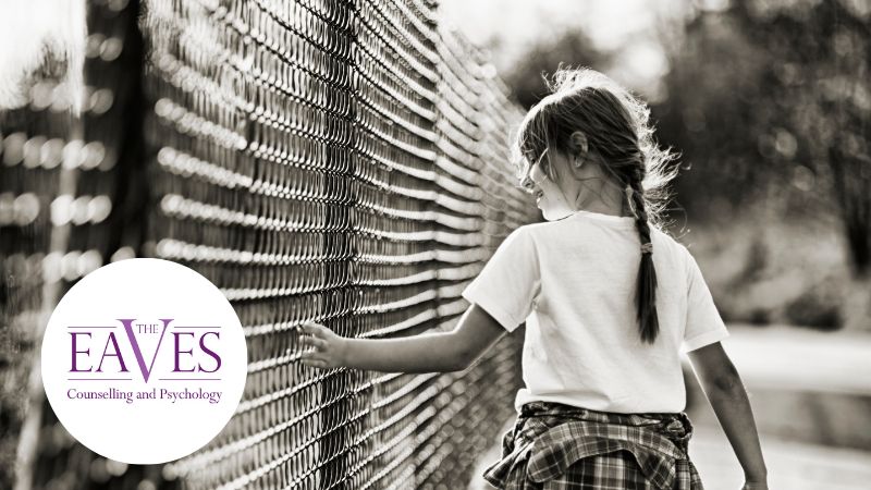 Child walking alone along a long fence, hand gliding along the panels, symbolising isolation and childhood trauma.