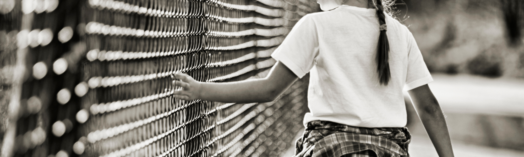 Child walking alone along a long fence, hand gliding along the panels, symbolising isolation and childhood trauma.