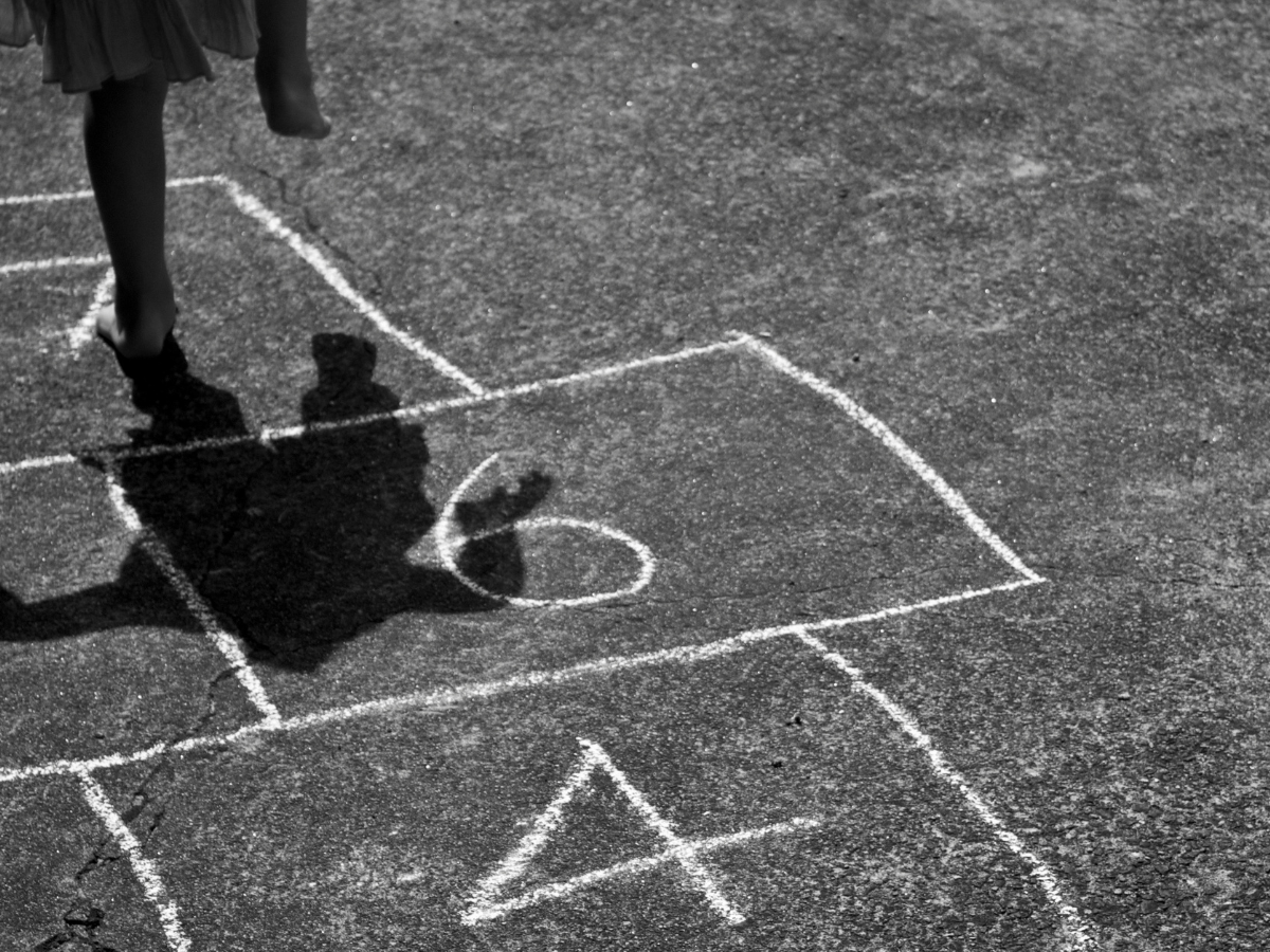 Child playing hopscotch on the pavement, hopping between numbered chalk squares.