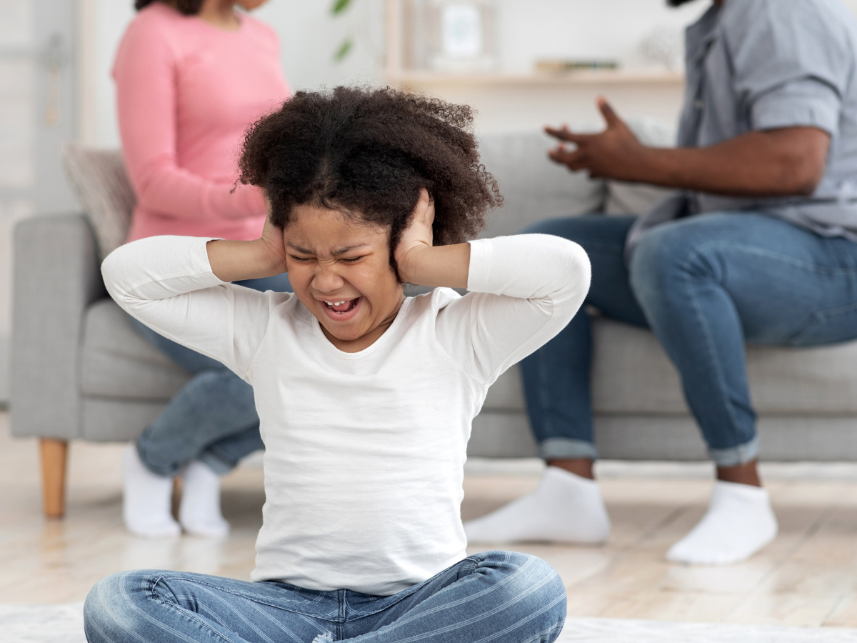 Child covering ears in distress while parents argue in the background, illustrating the effects of childhood trauma.