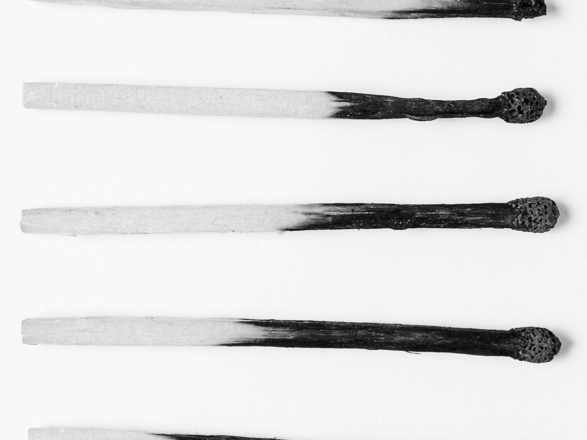 Half of a matchstick used and burnt out, next to a fresh, unused matchstick, symbolizing burnout and exhaustion