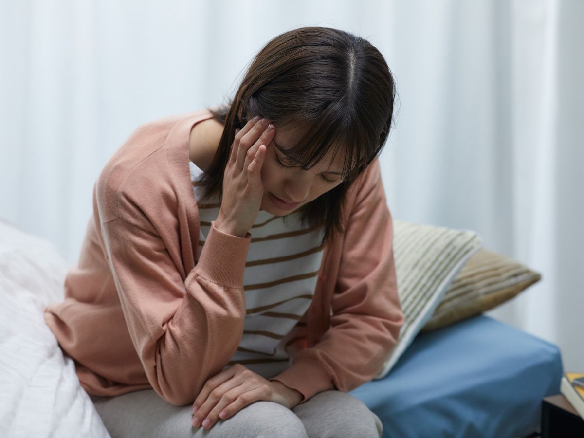 Woman sitting on bed with head in hands, appearing overwhelmed and anxious, symbolizing OCD or perfectionism stress
