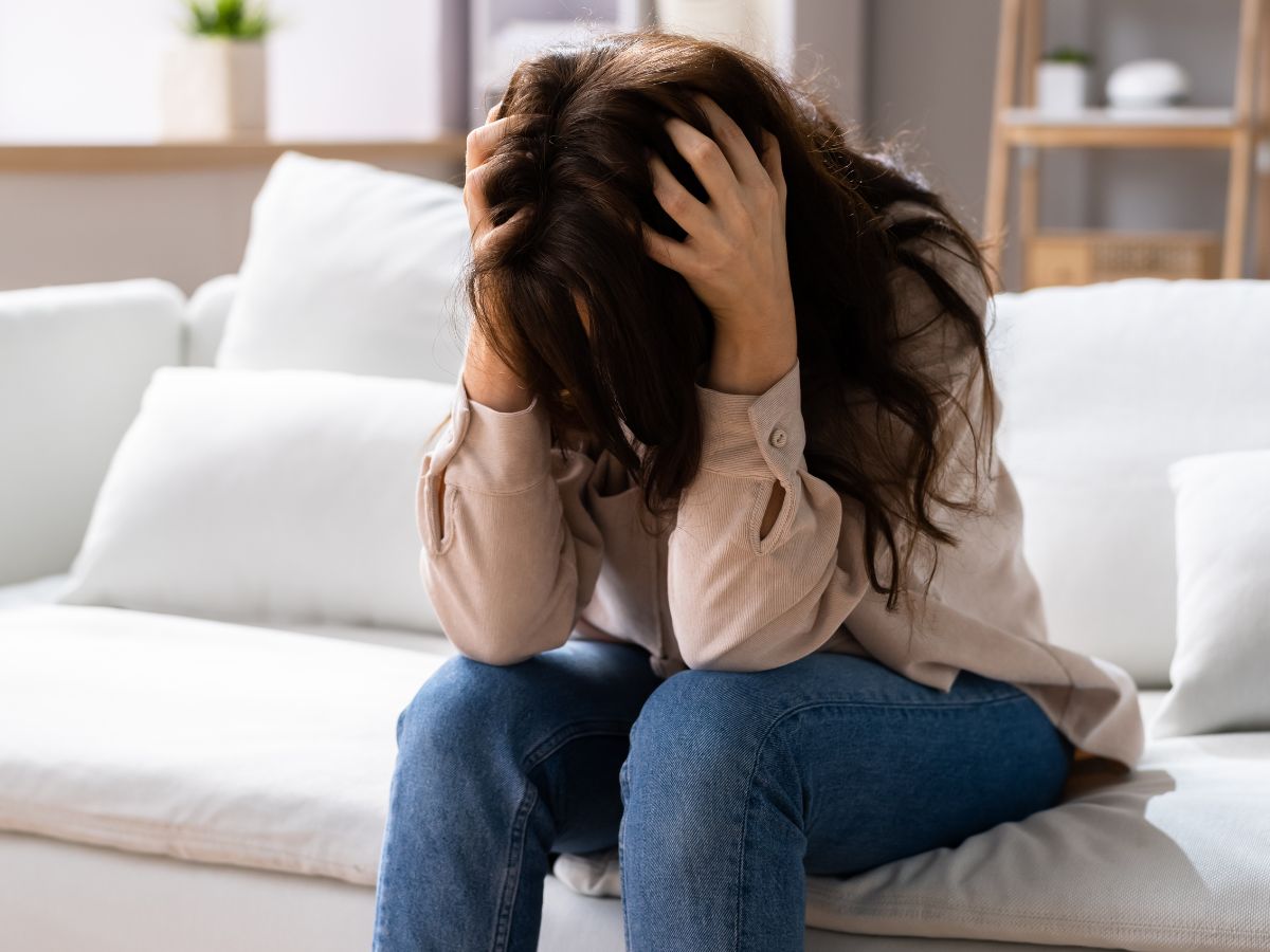 A distressed woman sitting on a sofa, holding her head in her hands, symbolising the overwhelming anxiety and intrusive thoughts often linked to OCD.
