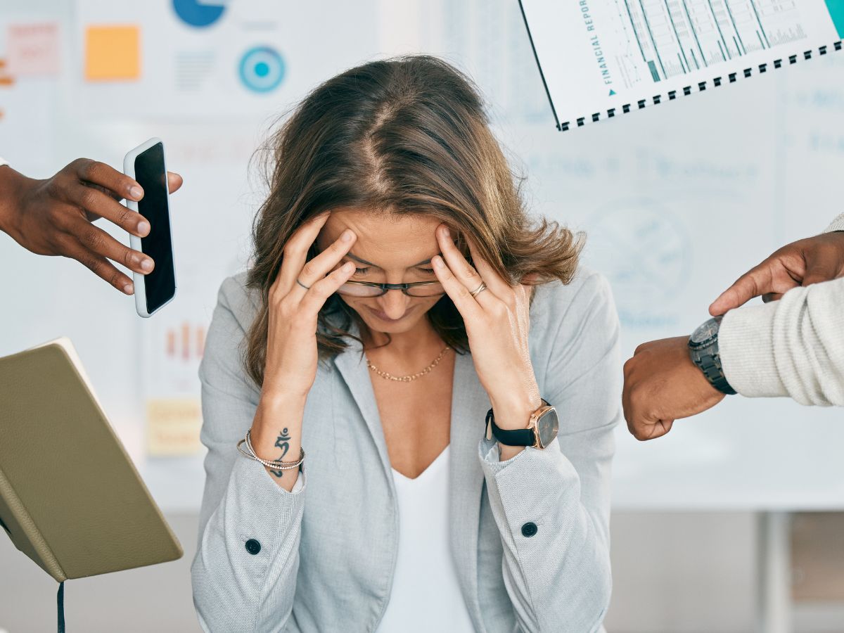 Stressed woman at desk surrounded by phones, schedules, and deadlines, overwhelmed by demands