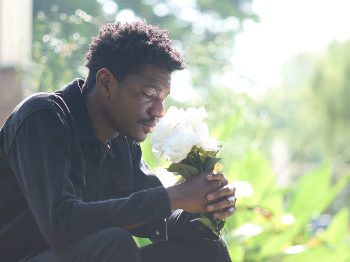 Man sitting outdoors holding a bouquet of white flowers, reflecting in grief and remembrance.