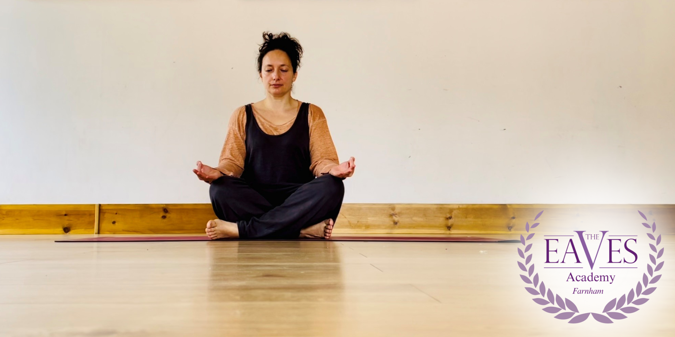 Woman sitting cross-legged in a peaceful yoga pose with The Eaves Academy Farnham logo in the corner, promoting New Beginnings Yoga in Farnham.