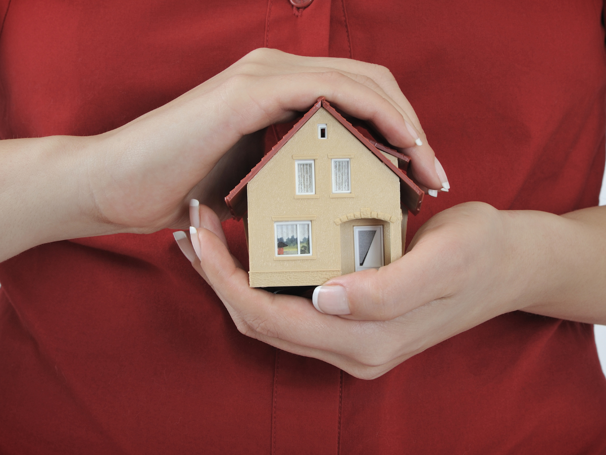 Woman in red shirt holding a house in front of her chest, symbolizing personal values and creating a safe, aligned life.