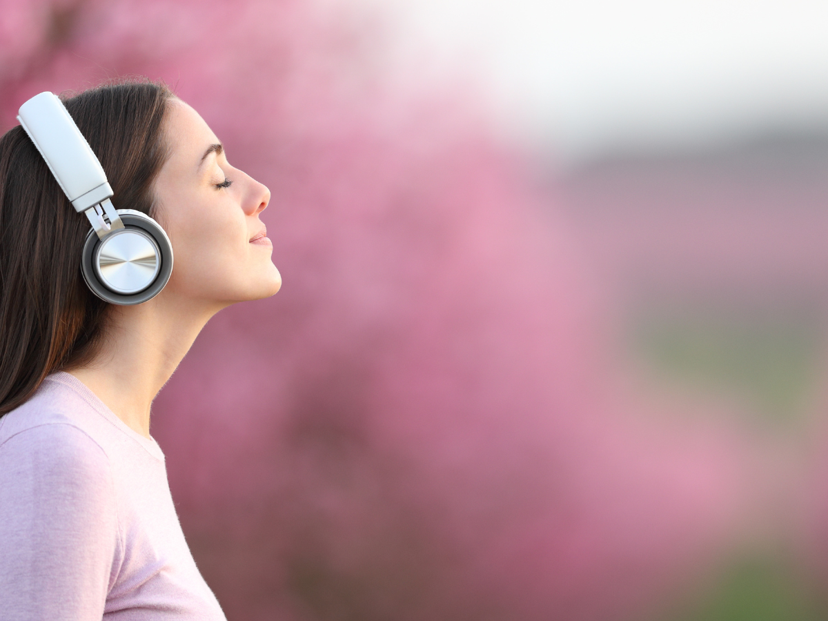 Woman wearing headphones, eyes closed with a faint smile, enjoying a moment of calm and mindfulness outdoors