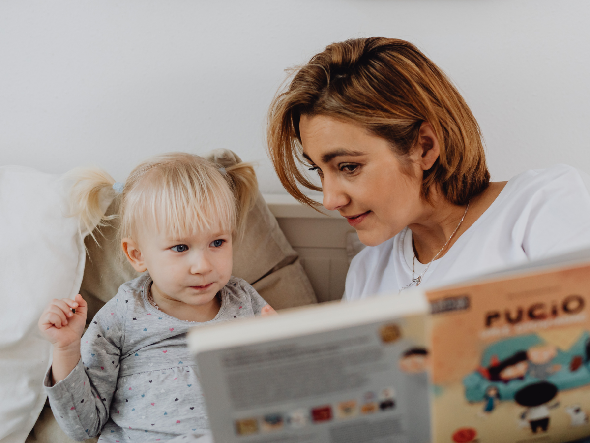 A mother and her child sitting on a bed, reading a book together, sharing a warm and joyful moment.
