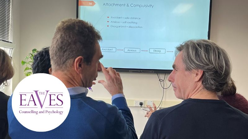 Two male therapists attending a Counselling CPD workshop, discussing insights with a presentation screen in the background