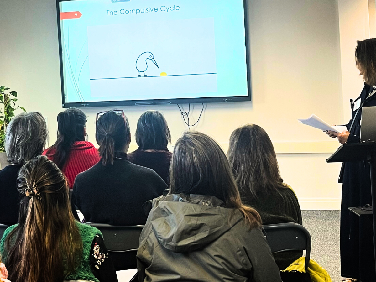 Group of therapists attending a Counselling CPD workshop, with presenter at the front reviewing notes and a presentation screen visible