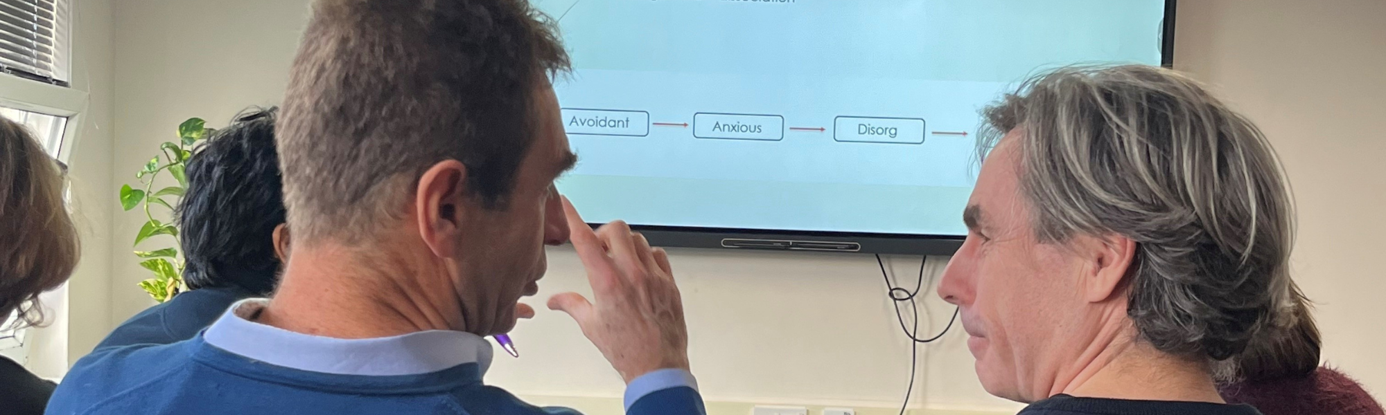 Two male therapists attending a Counselling CPD workshop, discussing insights with a presentation screen in the background