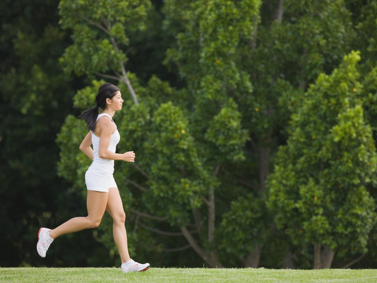 Woman running outdoors in a tree-filled landscape, boosting energy and reducing stress