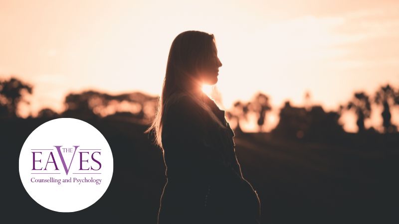 Silhouette of a woman looking away at a glowing sunset over a forested landscape, symbolising self-reflection and building self-esteem.