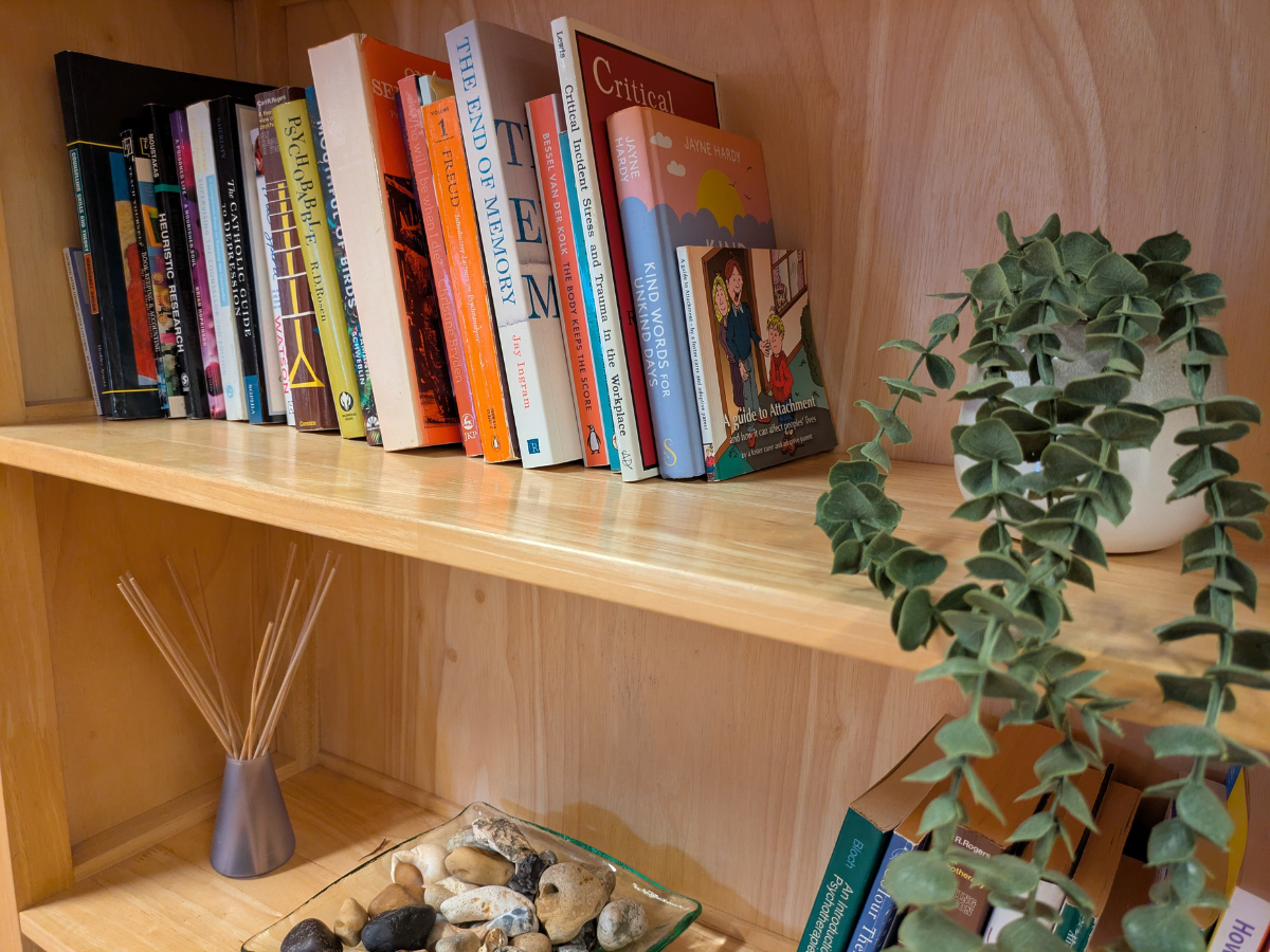 Alt Text: Cosy brown bookshelf with books, plant, and decorative shells in a therapy room