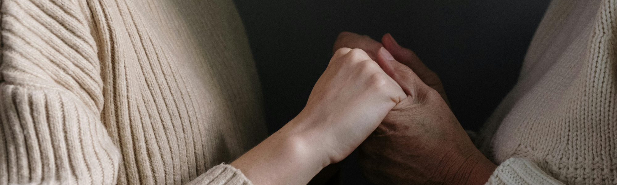 Two women, one middle-aged and one older, standing close together and holding hands in a supportive gesture, representing emotional connection and reassurance.