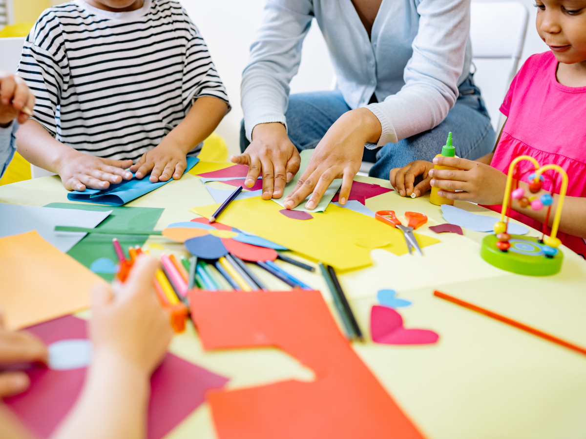 Adult and children doing arts and crafts together at table with coloured paper and pencils, supporting creativity and emotional expression