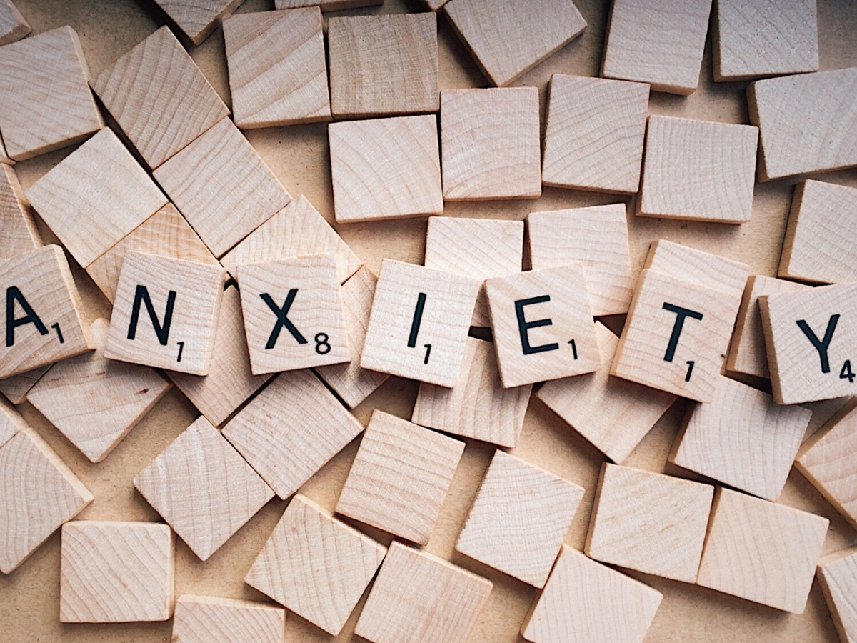 Scrabble tiles spelling “anxiety” placed on top of a pile of blank wooden tiles.