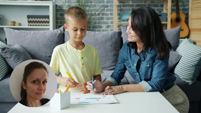 Mother kneeling with young son drawing together at coffee table in living room, supporting child’s emotional expression at home