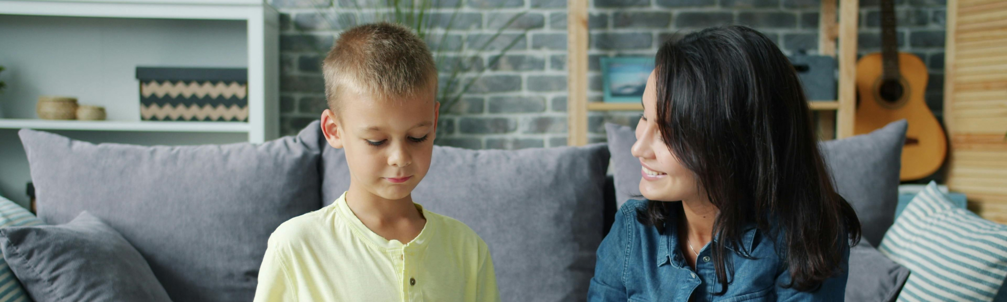 Mother kneeling with young son drawing together at coffee table in living room, supporting child’s emotional expression at home