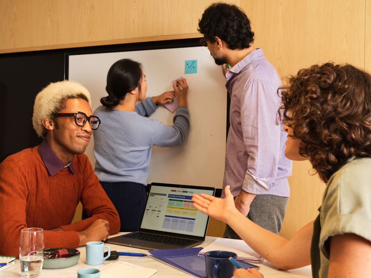 Employees collaborating in a meeting with a whiteboard and sticky notes, supporting workplace mental health and team communication in a Surrey business.