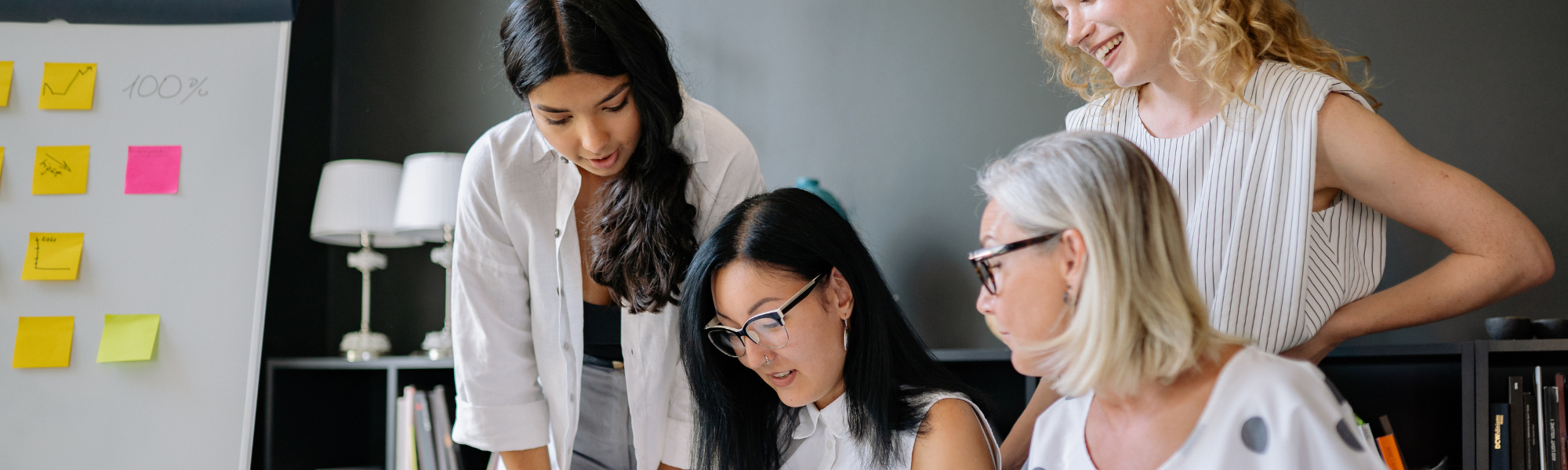 Employees collaborating around a table with a bookshelf and whiteboard in the background, highlighting workplace mental health support and team discussion.