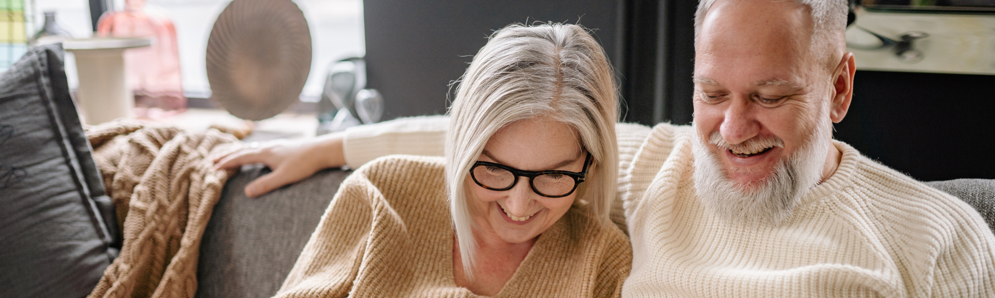 Elderly couple sitting together on a sofa, laughing warmly and enjoying a happy moment at home.