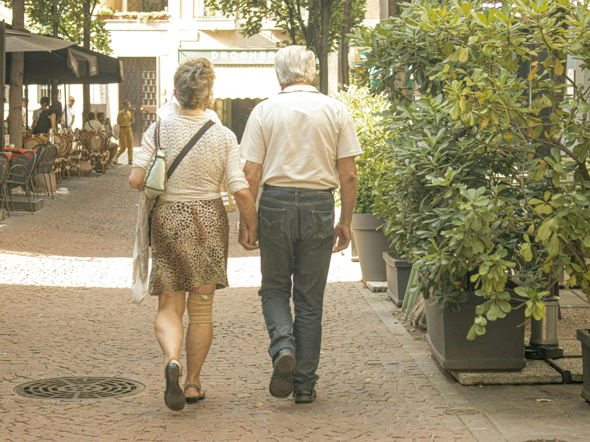 Elderly couple walking hand in hand along a sunlit street, enjoying time together outdoors.
