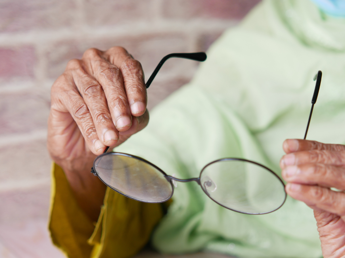 Close-up of an older person’s hands holding a pair of glasses.