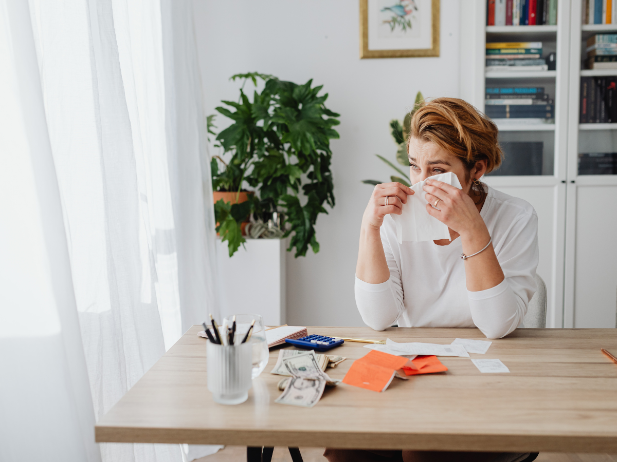 Woman sitting at a table feeling overwhelmed by financial stress and emotional distress, highlighting the impact of anxiety on wellbeing.
