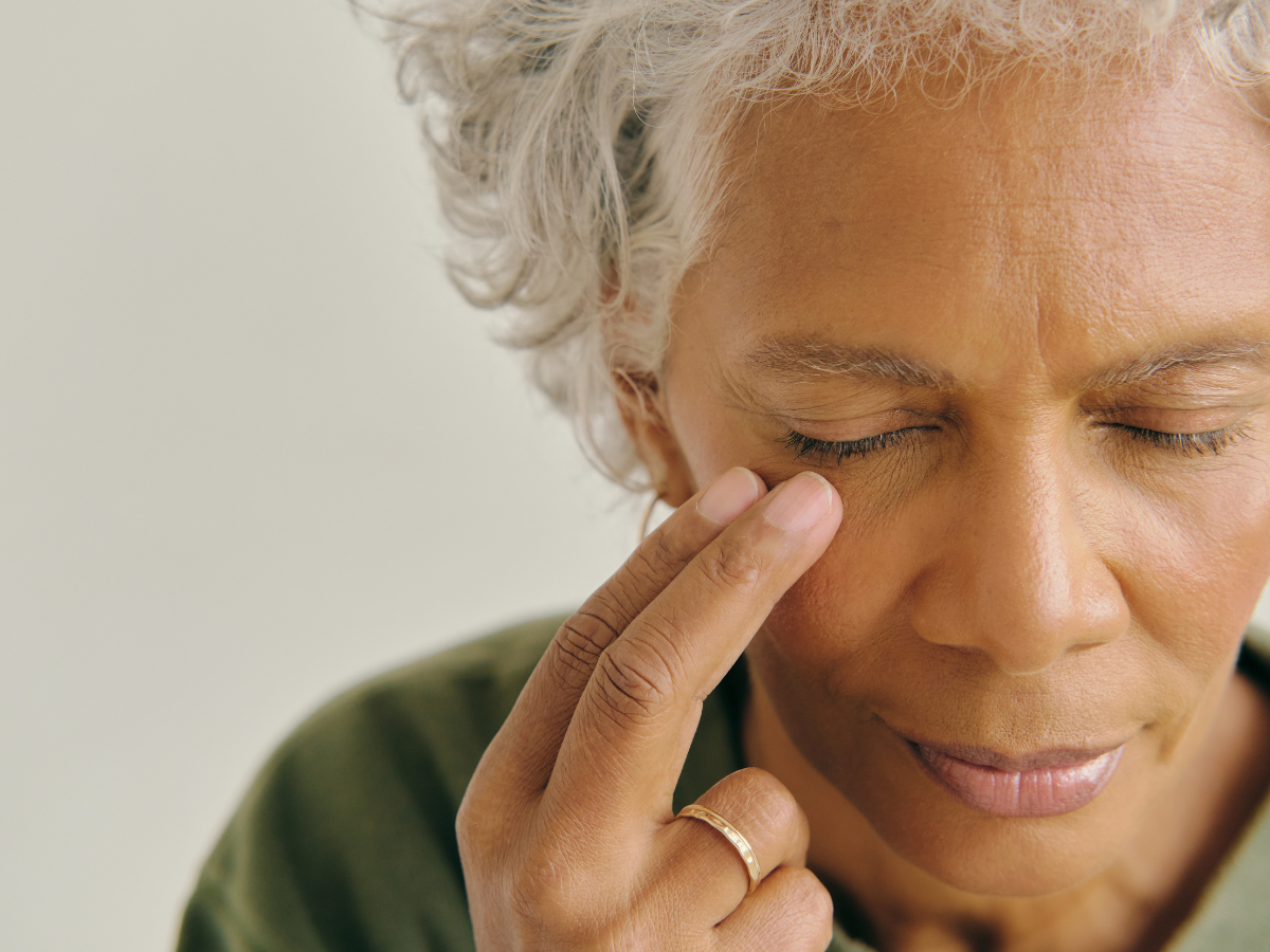 Older woman touching her temple with her eyes closed, experiencing emotional distress